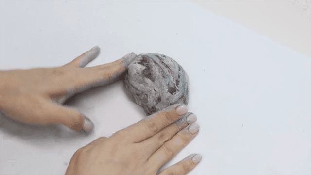 Hands shaping clay on a white surface