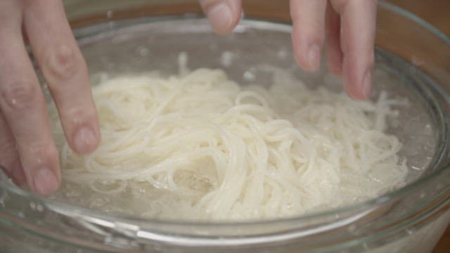 Hands rinsing noodles in a bowl of cold water