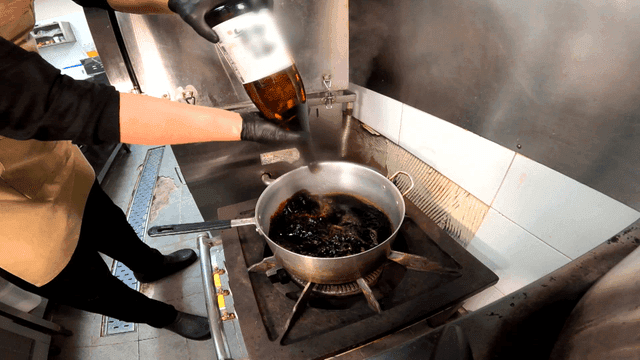 Chef pouring sake into pot of soy sauce on stove