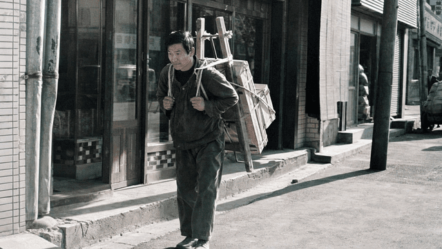Man carrying heavy load on his back in 70s