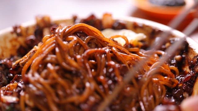 Noodles in thick black bean sauce being mixed with chopsticks