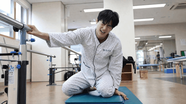 Young man wearing hospital gown sitting slumped in rehabilitation exercise room