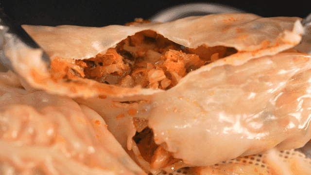 Kimchi dumpling being opened with tongs