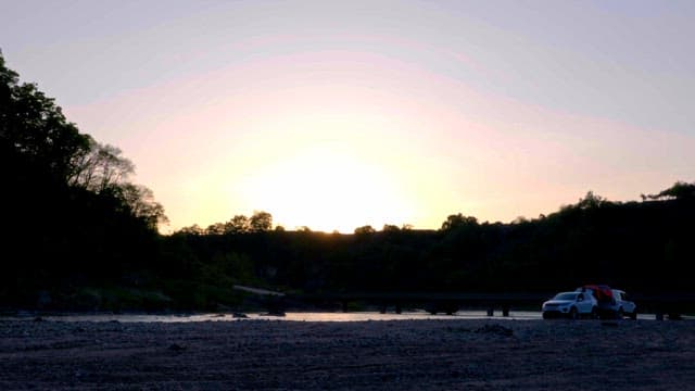 Sunset over a serene river with parked cars