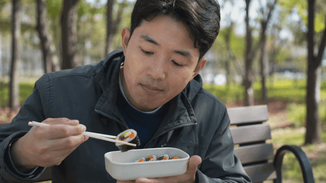 Man eating gimbap on park bench