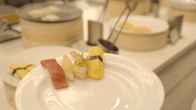 Person using tongs to place sushi on plate at buffet.