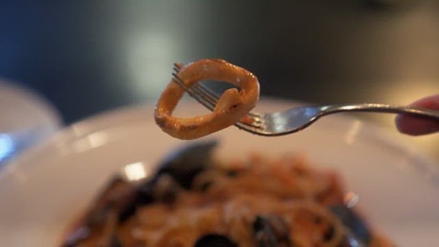 Person picks up a piece of squid from seafood pasta at a restaurant