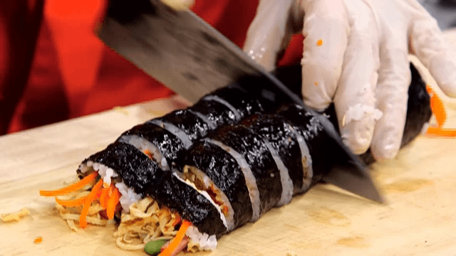 Gimbap being sliced on a wooden board