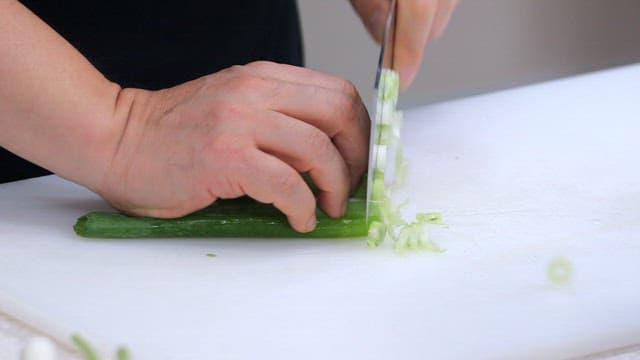 흰 도마 위에서 칼로 신선한 파를 자르는 모습
