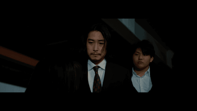 Two men in suits staring at a woman with her mouth taped