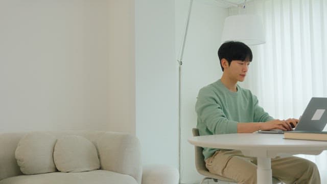 Man using laptop at living room table in bright interior