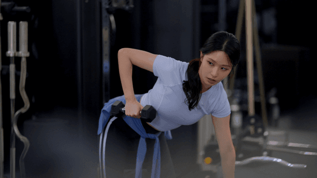 헬스장에서 덤벨 로우 운동을 하는 젊은 여성