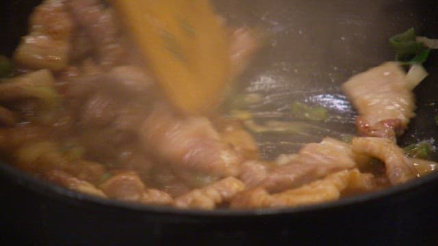 Cooking pork belly in a hot pan with wooden spoon