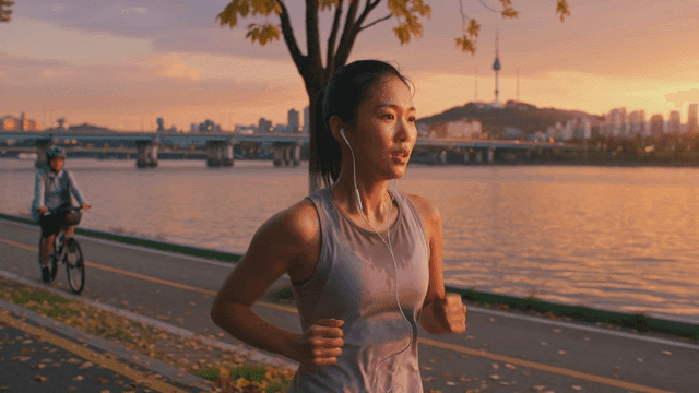 Woman jogging along riverside path at sunset