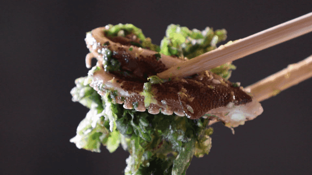 Fresh octopus and greens held by chopsticks
