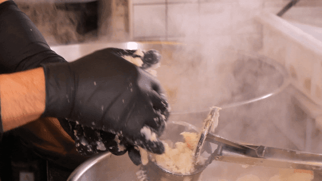 Chef putting mashed potatoes into masher in steaming kitchen