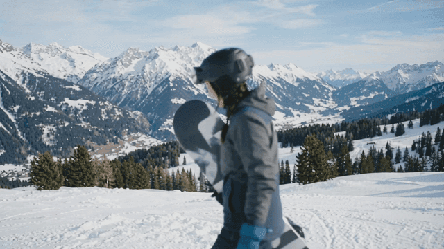 Woman holding snowboard on snow-covered mountain