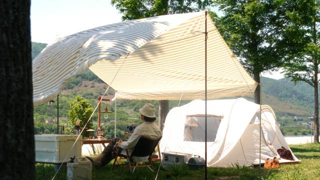 Person resting under the shade of a tarp installed on green grass