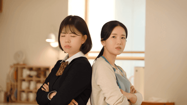 Mother and daughter standing back to back at home