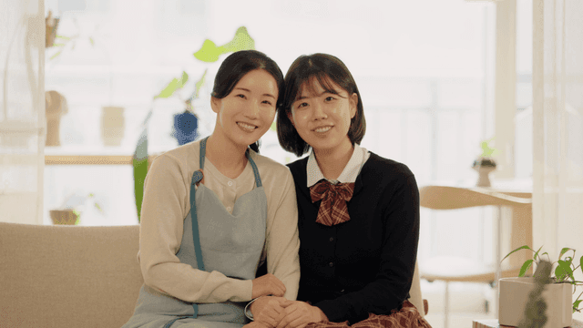 Mother and daughter sitting on sofa, looking straight ahead and smiling