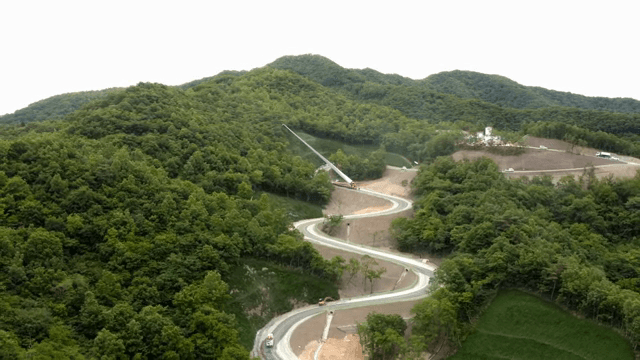 울창한 숲 속 구불구불한 도로에서 풍력 터빈 자재를 운반하는 모습