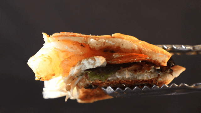 Tongs lifting sandwich filled with shrimp and vegetables