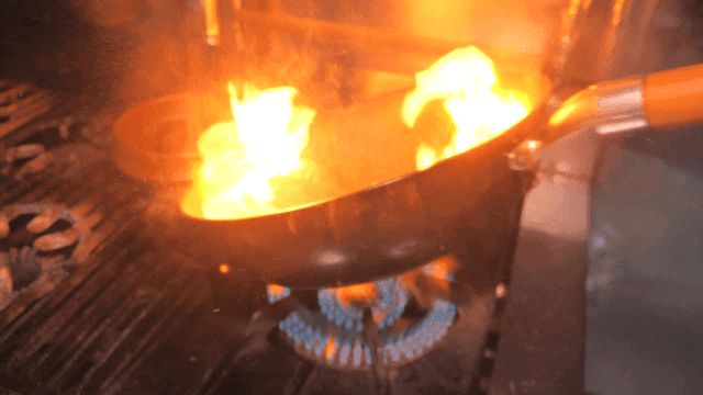 Flames rise as meat is fried in pan