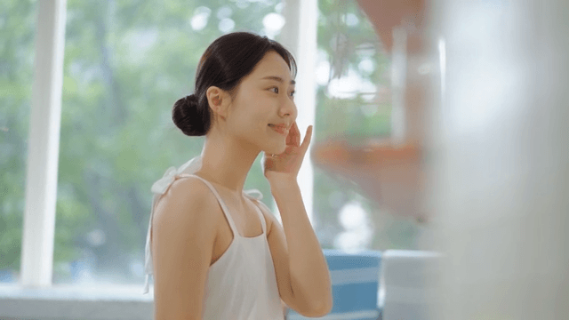 Woman in white clothes smiling and touching her face in a bright room