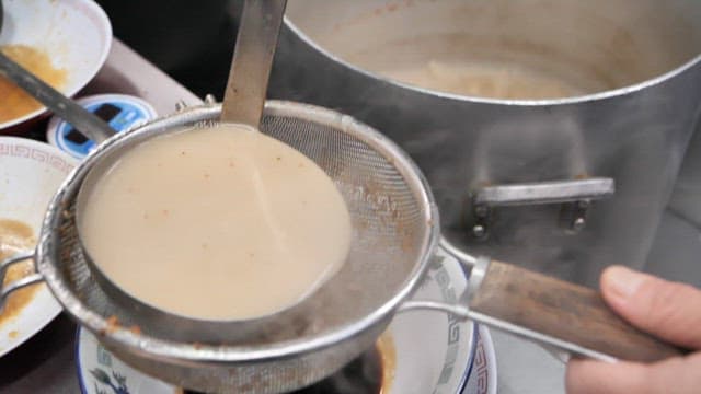 Pouring hot soup broth through a strainer into a bowl