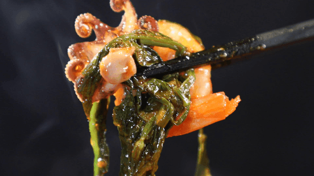 Chopsticks picking up baby octopus and shrimp from seafood stew