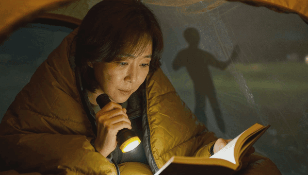 텐트 안에서 손전등으로 책을 읽고 있는 여성