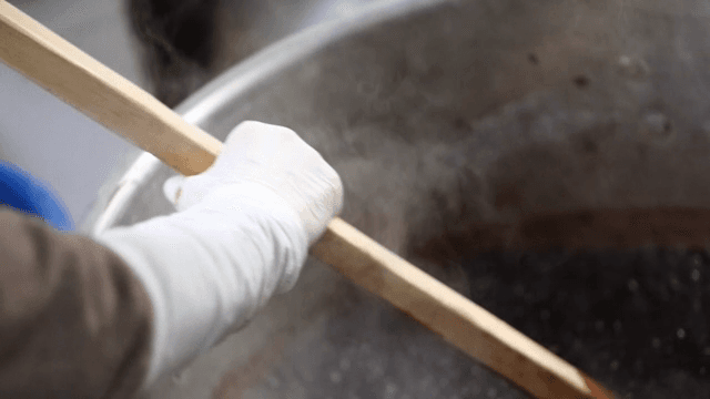Boiling red beans in a large pot with a wooden spatula