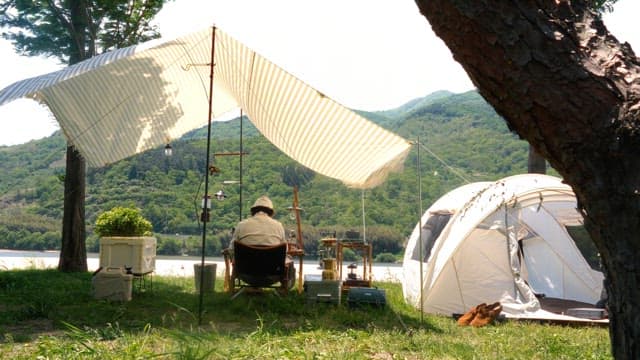 Person relaxing at a riverside campsite during a sunny day