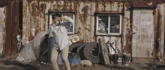 Man making a funny gesture in front of a rusty building