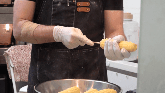 Inserting corn onto chopsticks by chef in kitchen