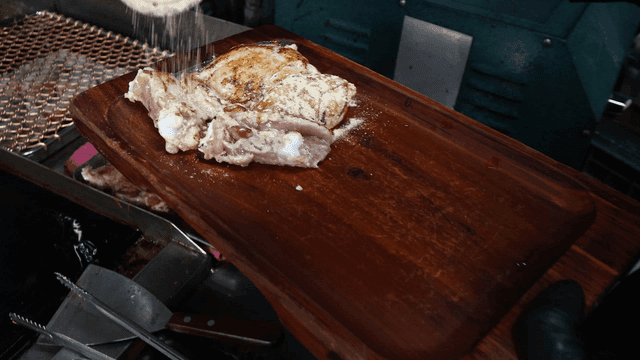 White powder sprinkled on raw chicken on wooden cutting board