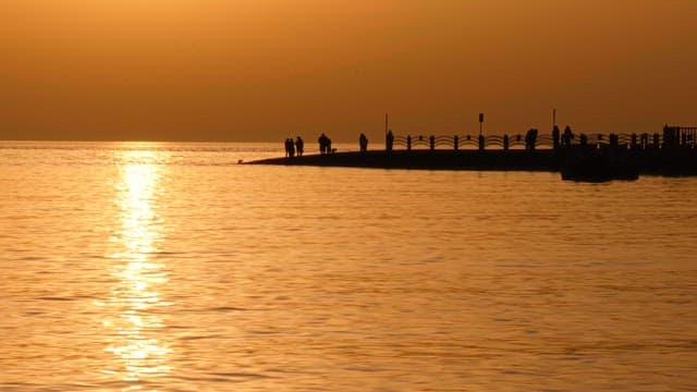 Sunset over a pier with people gathered and serene sea