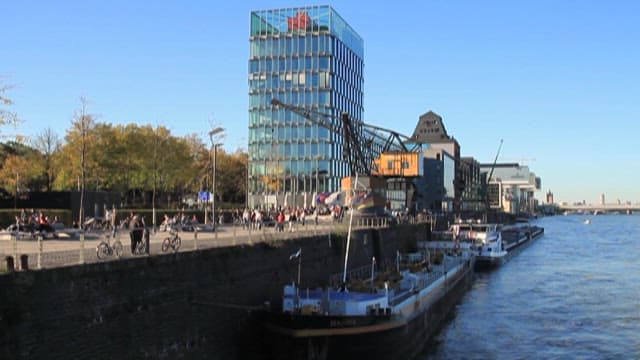 People walking along the riverside with cargo ships
