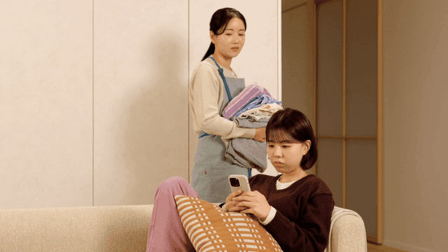 Mother watching her daughter using her smartphone on sofa