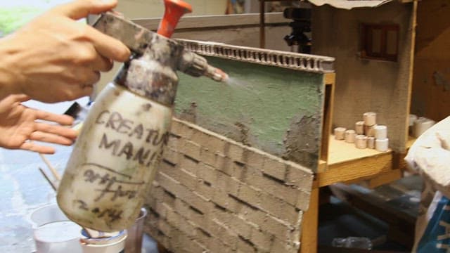모델 제작자가 미니어처 건물을 신중하게 페인팅하는 모습