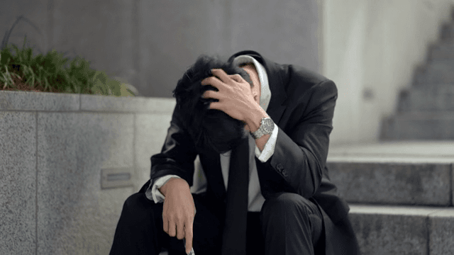 Office worker sitting on stairs looking at his phone in despair