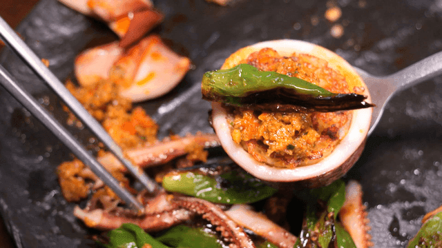 Chopsticks holding spicy ssamjang and grilled shishito peppers for squid sundae