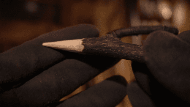 뾰족하게 조각된 막대를 들고 있는 장갑 낀 손