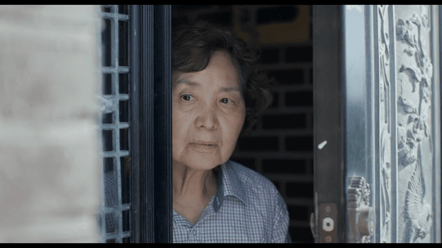 문을 통해 밖을 엿보는 노인 여성