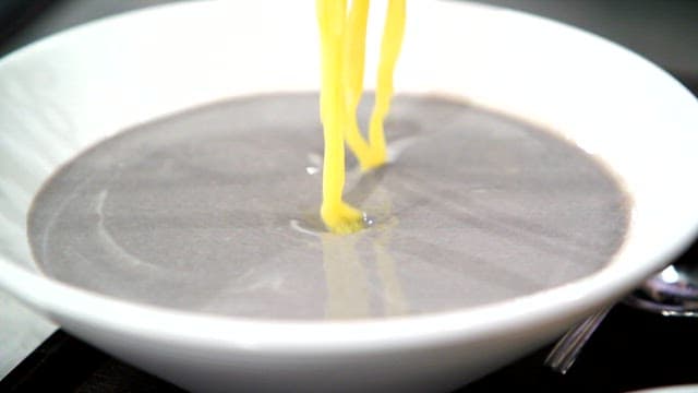 Yellow noodles being put in black soybean soup