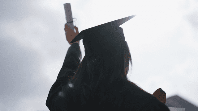 Graduates holding their diplomas under bright sky