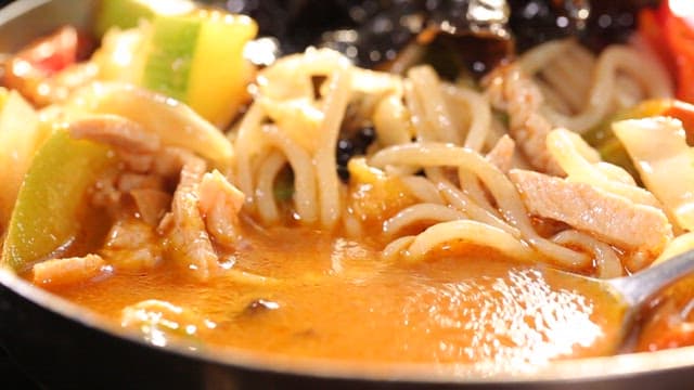 Spoonful of broth of spicy chili jjambbong with vegetables and meat