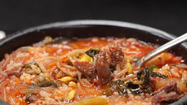 Spoonful of spicy Korean beef and rice soup served with sliced radish kimchi