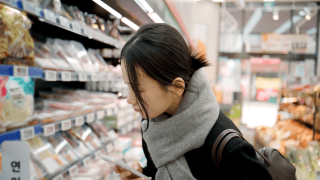 Young woman shopping while looking at her smartphone at supermarket
