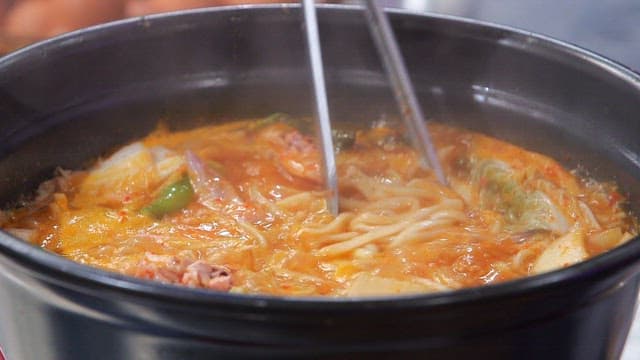 Noodles picked from the spicy noodle soup with chicken boiling in the pot